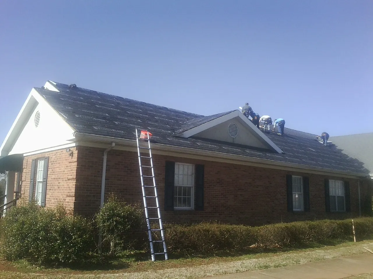 Crew tearing shingles off a brick ranch roof with a ladder set — Metal Roof Repair work by our crew in Elgin